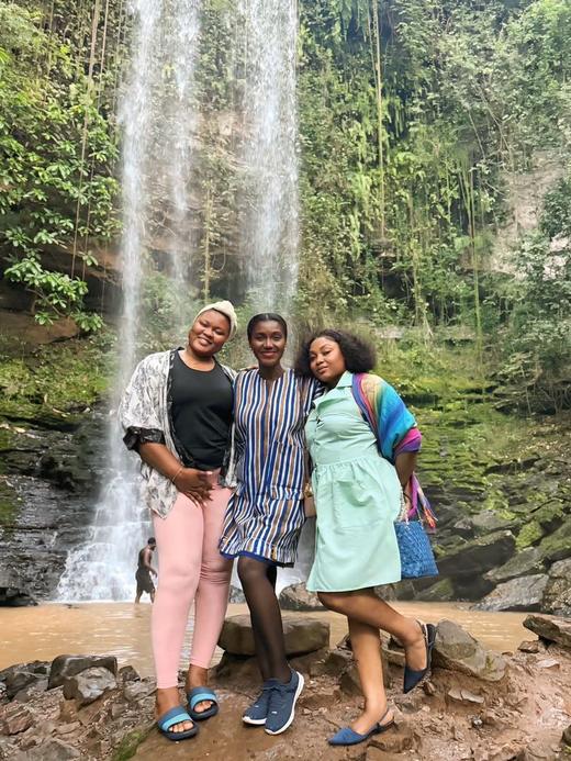 Three guests smiling in front of a forest waterfall.
