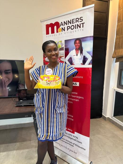 A guest waving and proudly holding her decorated cake beside the Manners on Point banner.