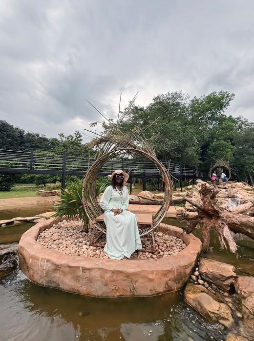 A guest seated inside a woven circular sculpture set in a garden pond.