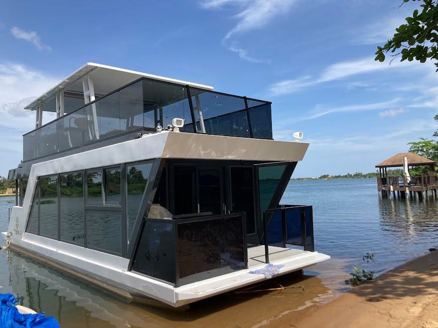 A two-deck glass-enclosed cruise boat moored at the riverbank.