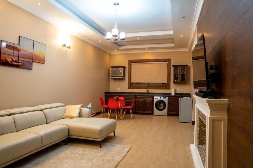 A suite living area with a sofa, kitchenette, dining table and large television.